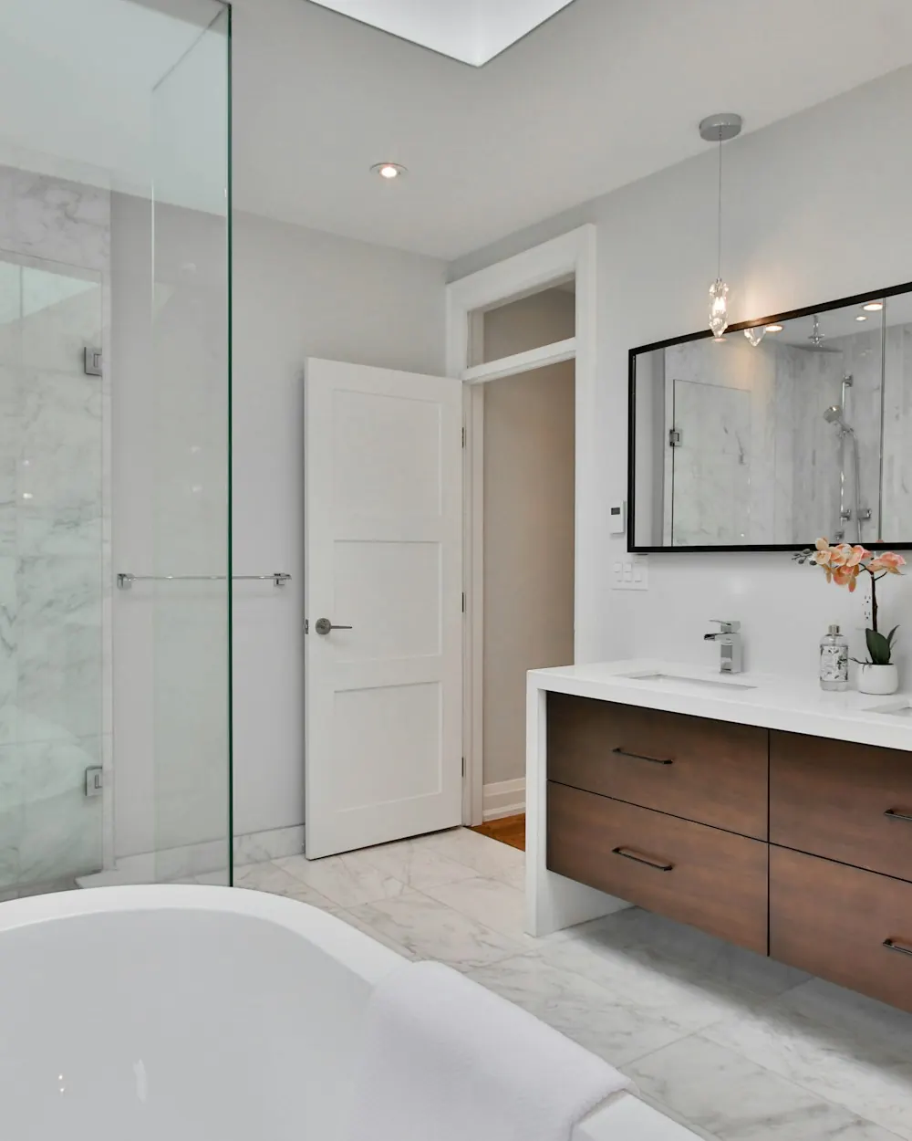 Bathroom with a frameless glass walk-in shower, freestanding tub and walnut double vanity