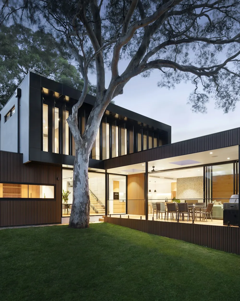 Modern renovated house at dusk with warm lights in floor-to-ceiling windows