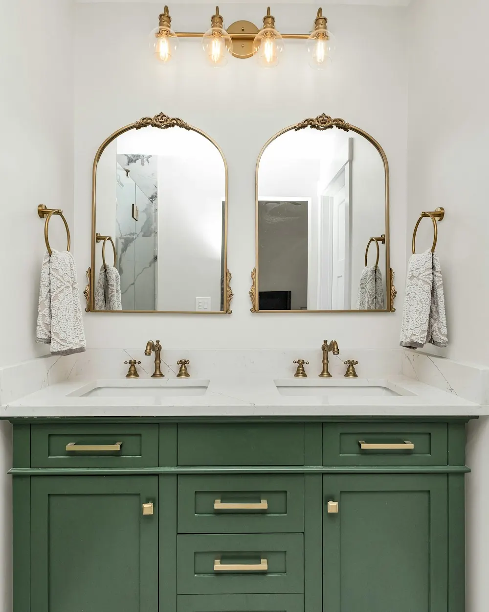 Bathroom with a green double vanity, marble walls and brass mirrors