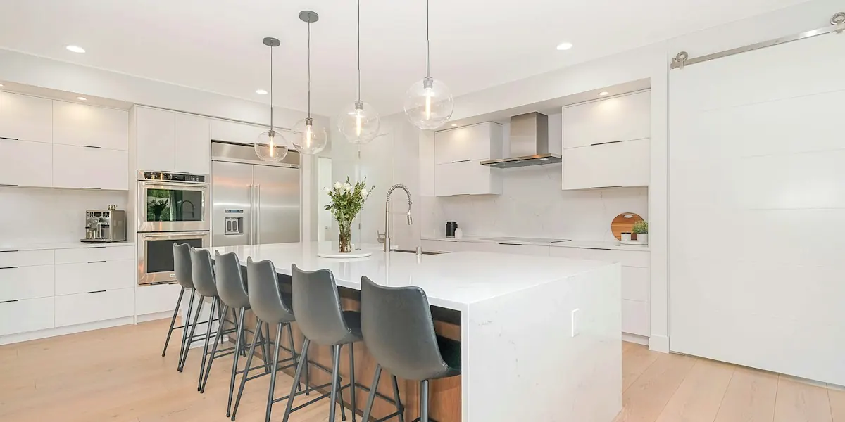 White kitchen remodel with a large island, gray bar stools and pendant lights
