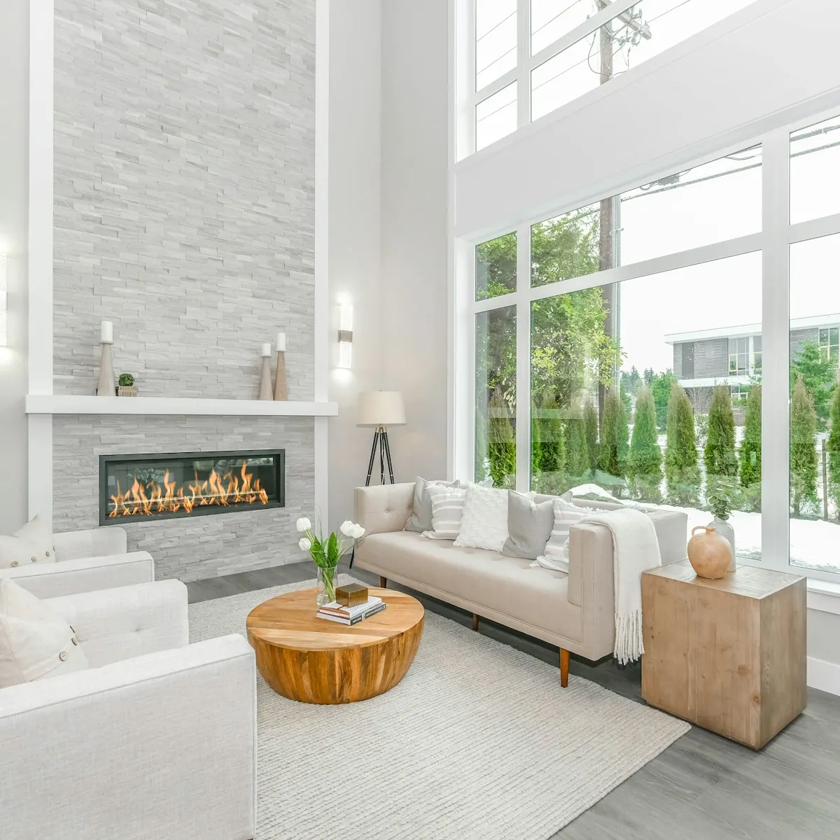 Bright renovated living room with double-height windows, a fireplace and white sofas